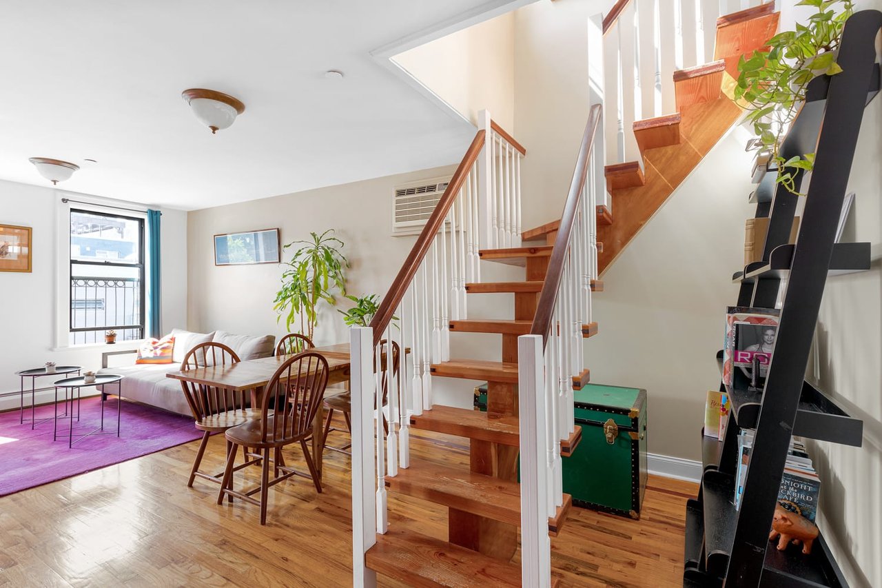 Living and dining area with a prominent wood staircase, white sofa, and purple rug.
