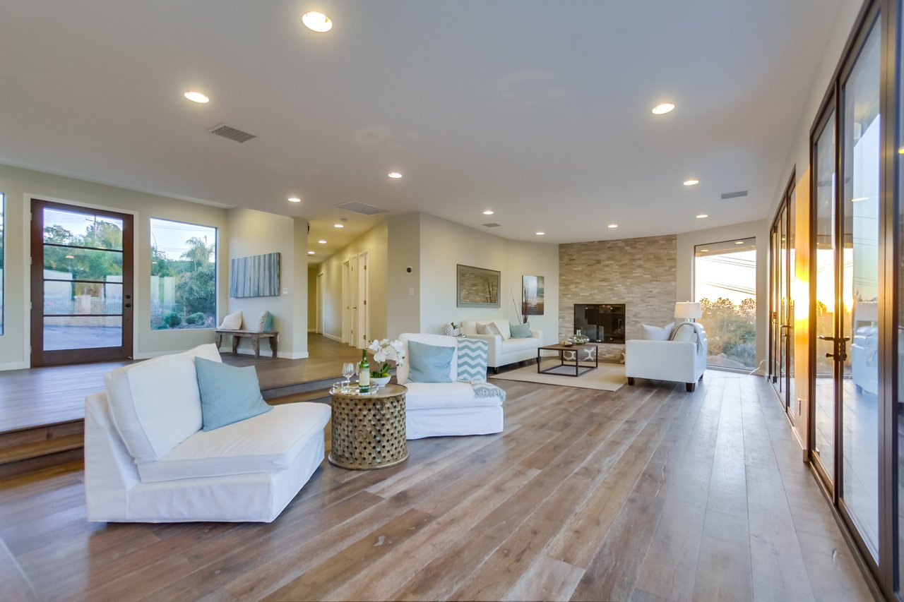 Furnished living room with white sofas, a stone fireplace, and floor-to-ceiling glass doors.