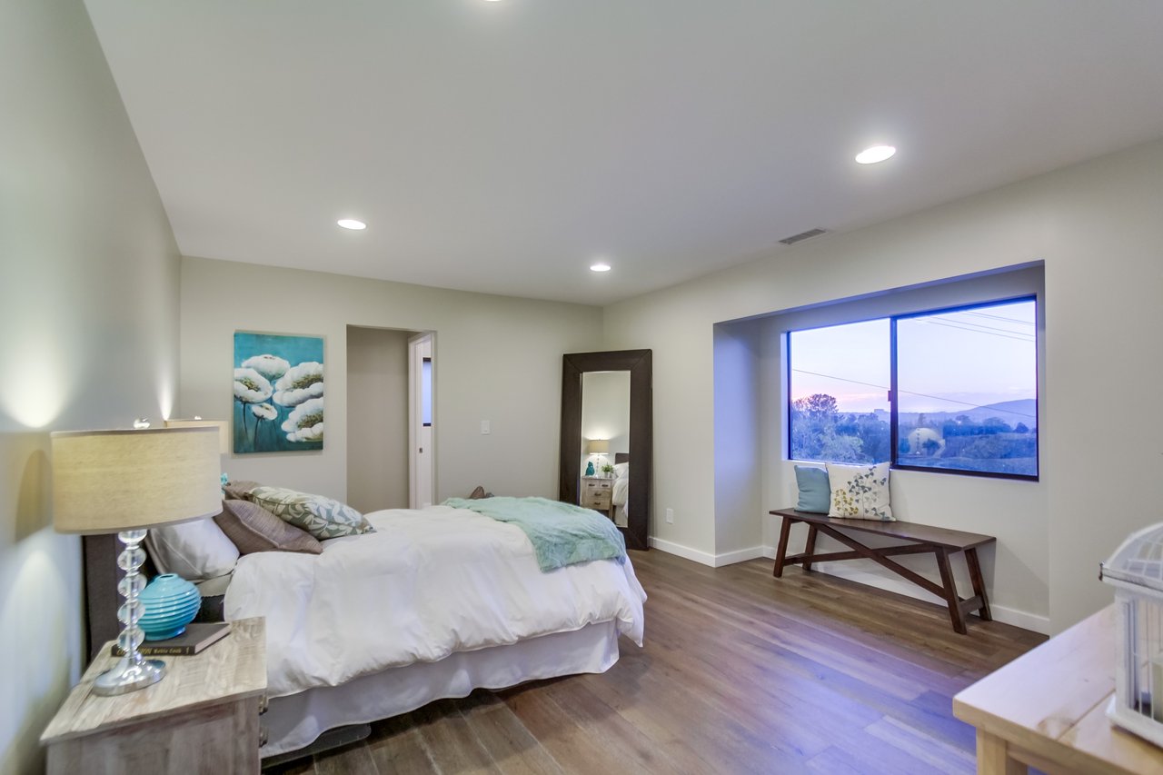 Bedroom with a large bed and a bench beneath a window overlooking distant hills.