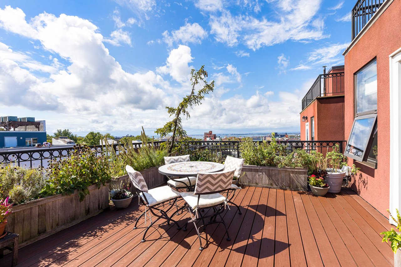 Rooftop terrace with a round dining table, raised planters, and distant water views.