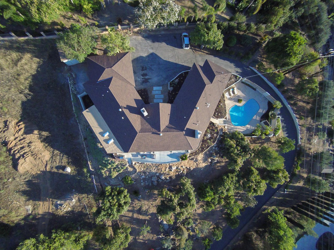 Aerial view of a large home with a curved swimming pool and tree-filled grounds.