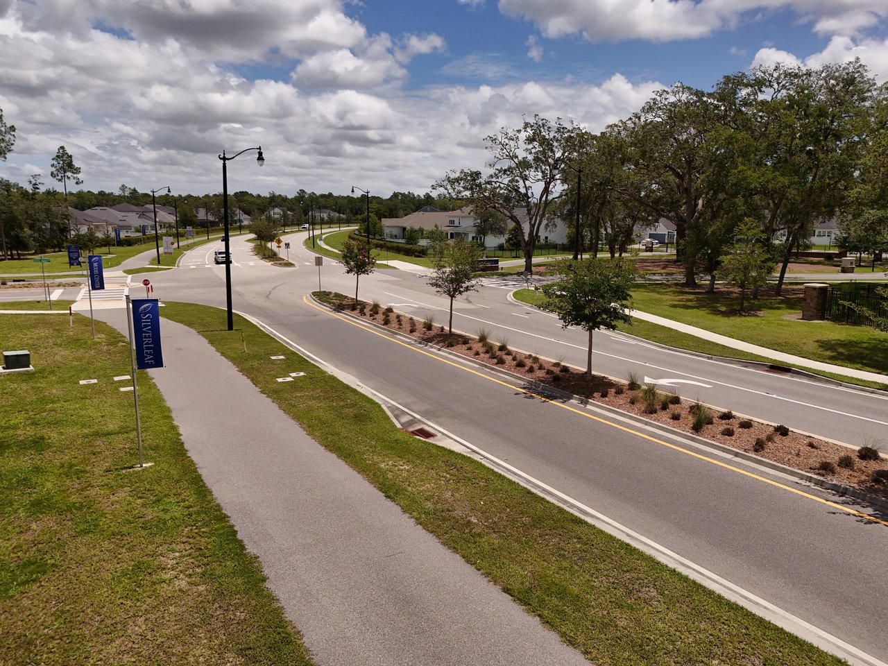 Silverleaf neighborhood entrance with curving roads, sidewalks, streetlights, and homes among mature trees.