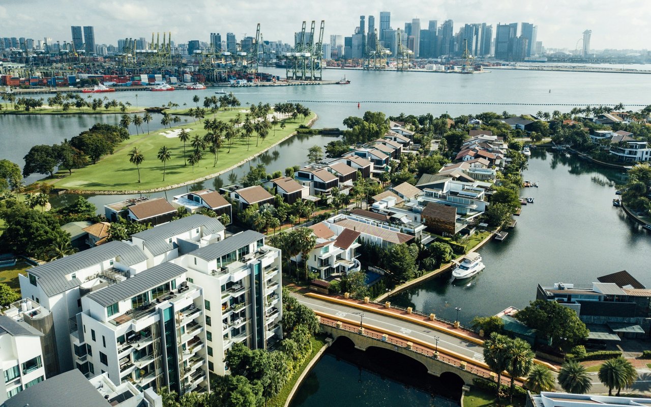 Waterfront neighborhood with canal-side homes, a green space, and a distant city skyline.