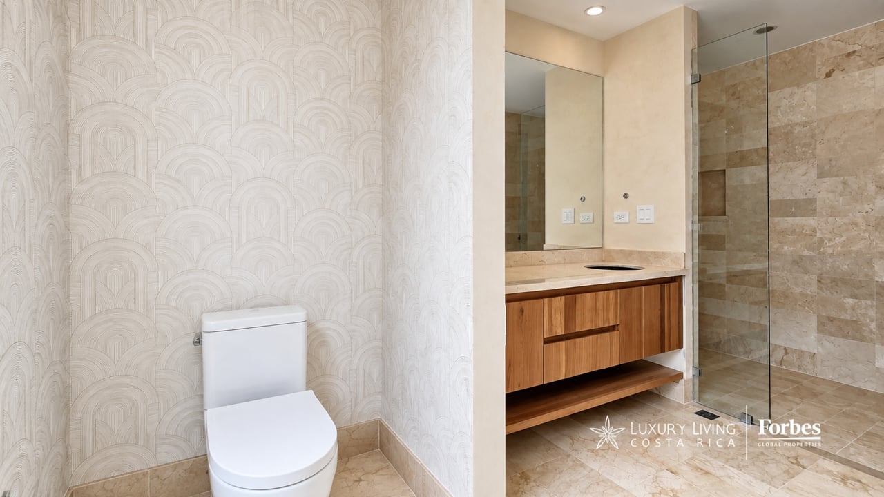 Penthouse bathroom with patterned wallpaper, a wood vanity, and a glass-enclosed stone shower.