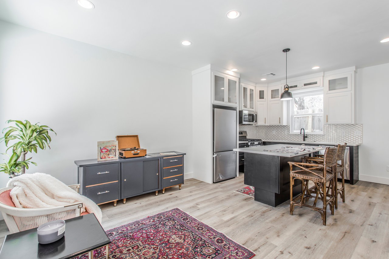 Bright kitchen with dark island, white cabinetry, hexagonal backsplash, and adjacent sitting area.