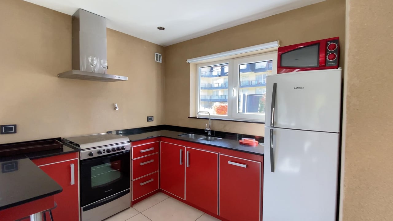 Kitchen with red cabinets and black countertops, a stainless-steel range, and a window overlooking apartment buildings.