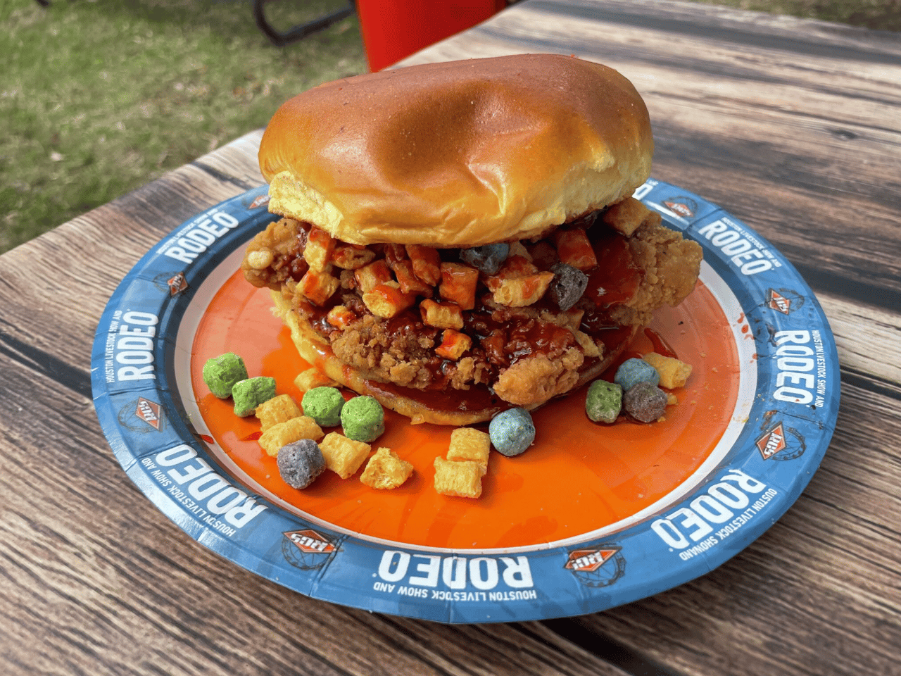 Rodeo fried chicken sandwich piled with colorful crunchy toppings on a branded plate.