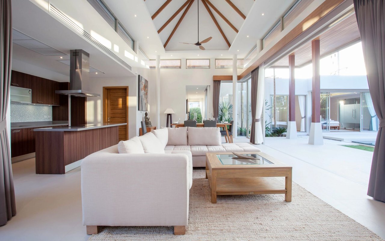 Open-plan living room with a white sectional, vaulted wood-beam ceiling, and glass doors to a courtyard.