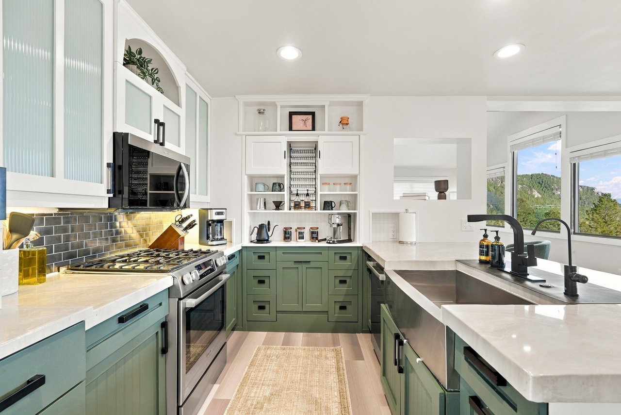Bright sage-green kitchen with a large island and wooded mountain views through broad windows.
