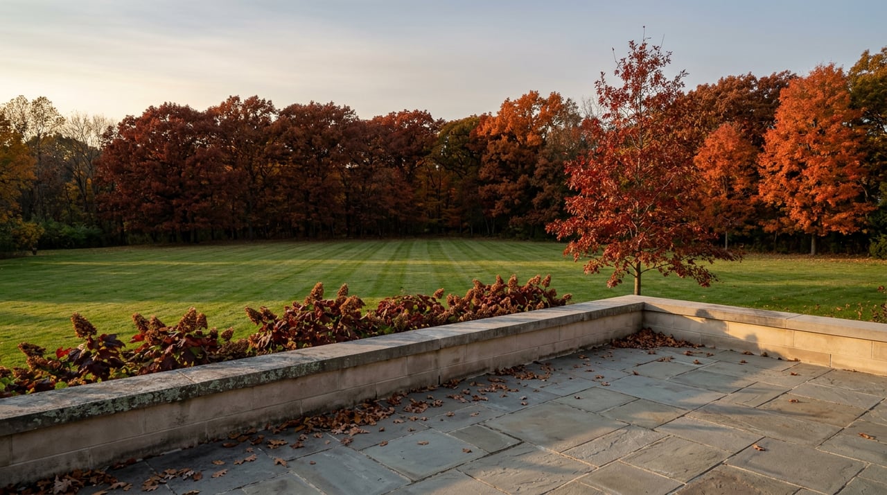 Stone terrace overlooks a broad striped lawn and dense red-orange autumn tree line.