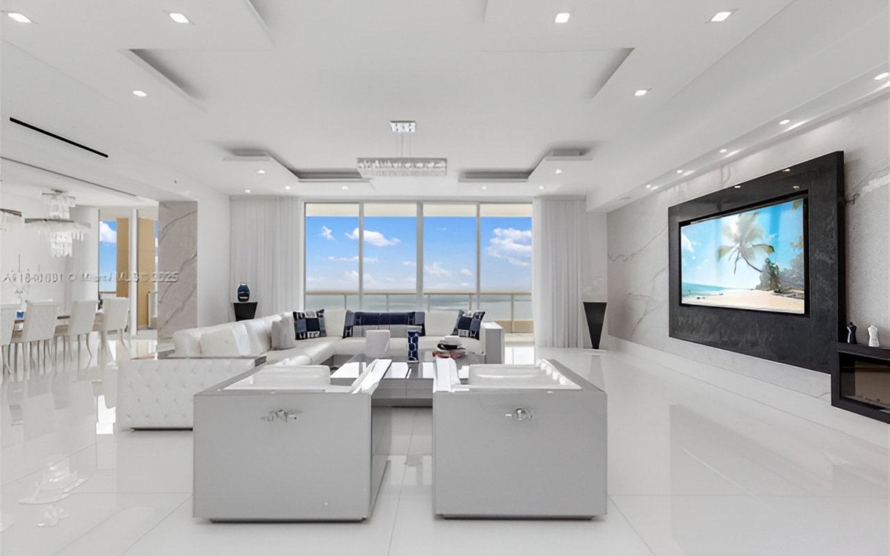 Luxury condo living room with white furnishings and floor-to-ceiling ocean-view windows.