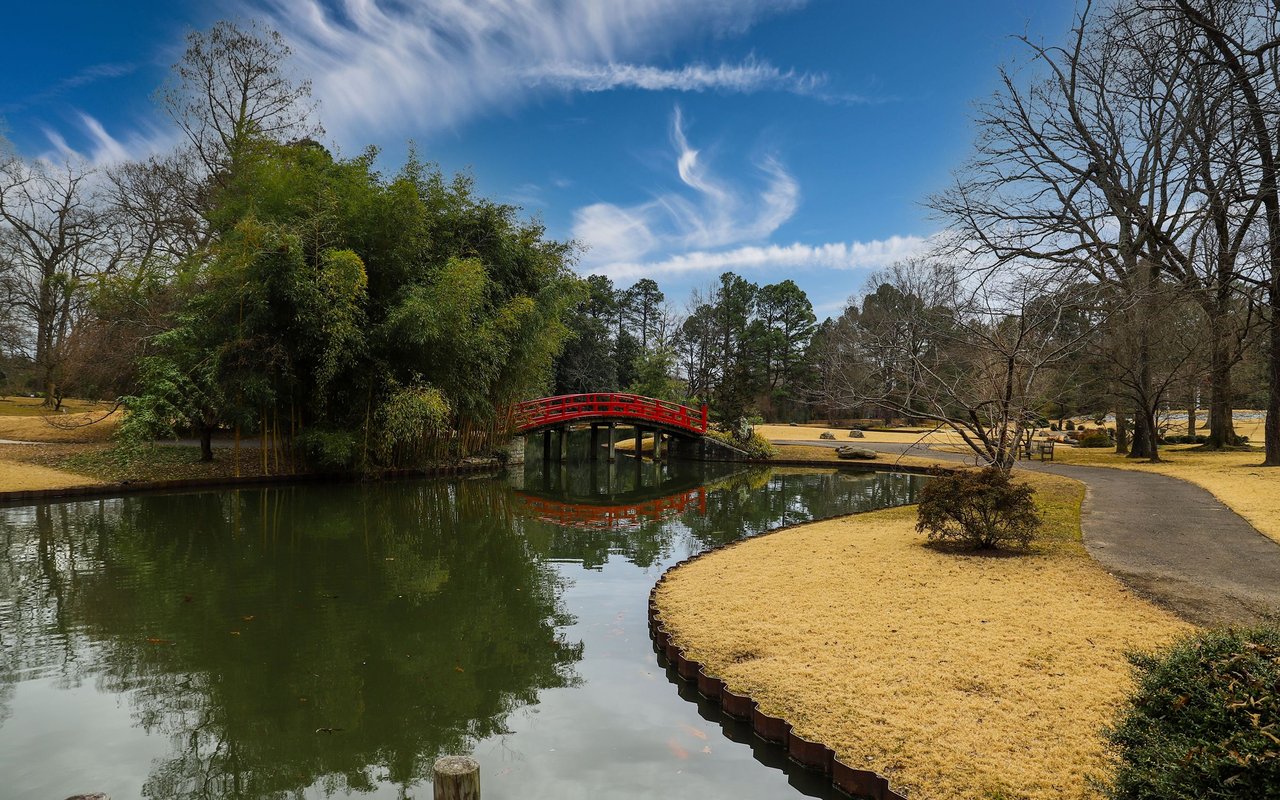 Park pond with a red footbridge, winding path, and leafless trees.