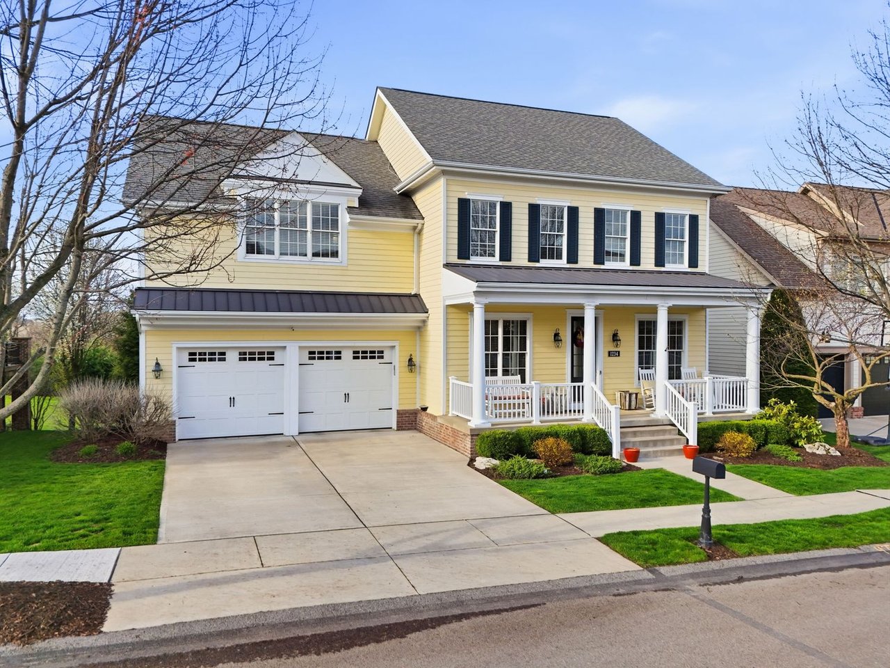Yellow two-story home with a covered porch, dark shutters, and a two-car garage.