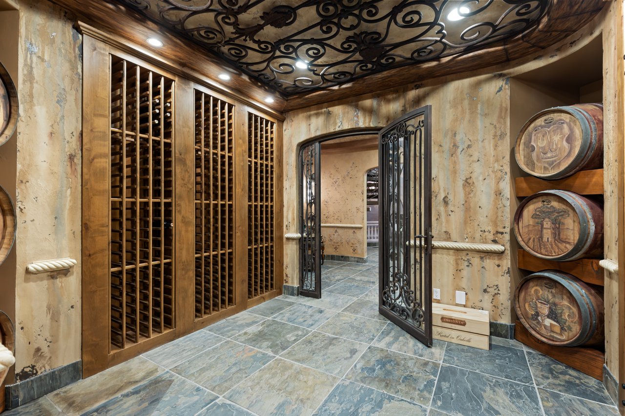 Wine cellar with tall wooden wine racks, stacked barrels, and ornate wrought-iron details.