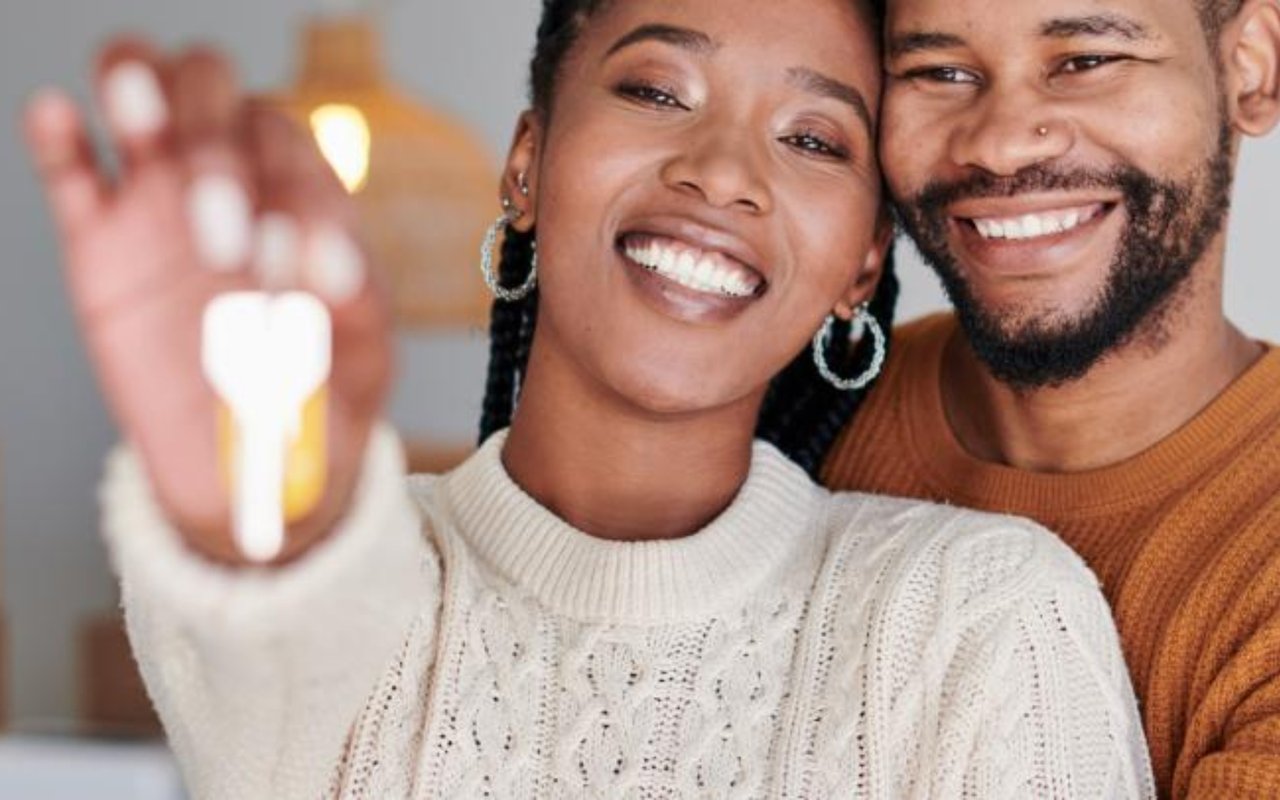 Smiling couple indoors, with the woman holding a house key toward the camera.