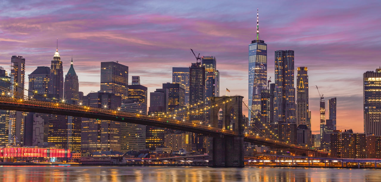 New York City skyline at dusk, with the illuminated Brooklyn Bridge and One World Trade Center.