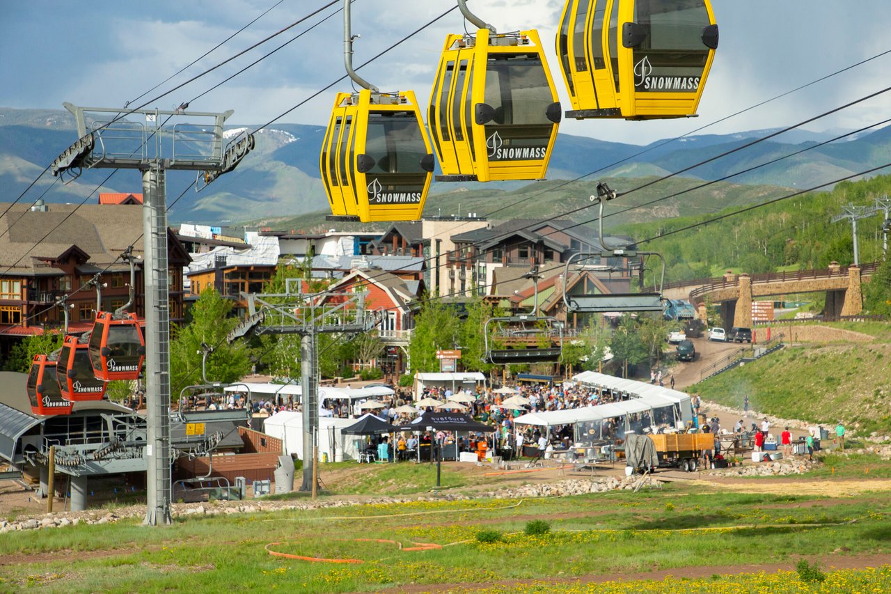 Yellow Snowmass gondolas pass above resort buildings and outdoor dining in summer.