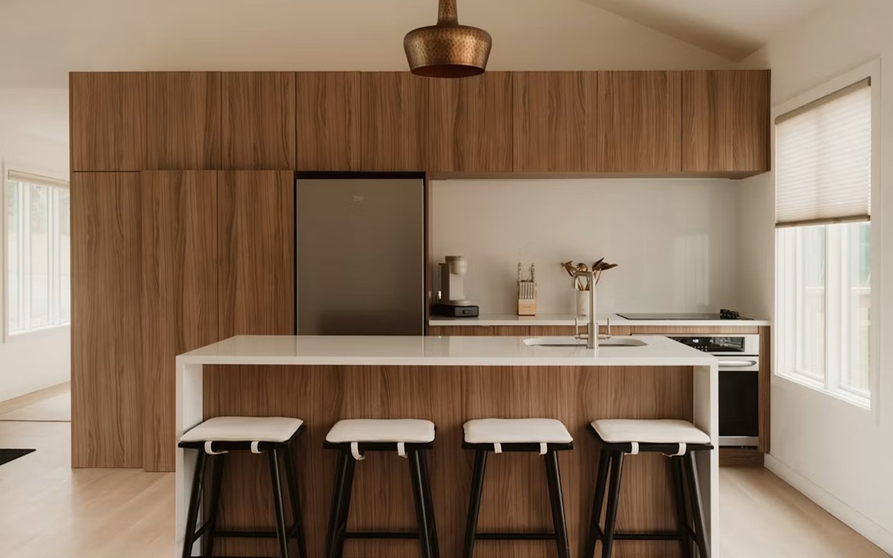 Modern kitchen with warm wood cabinetry, a white island, and four stools.