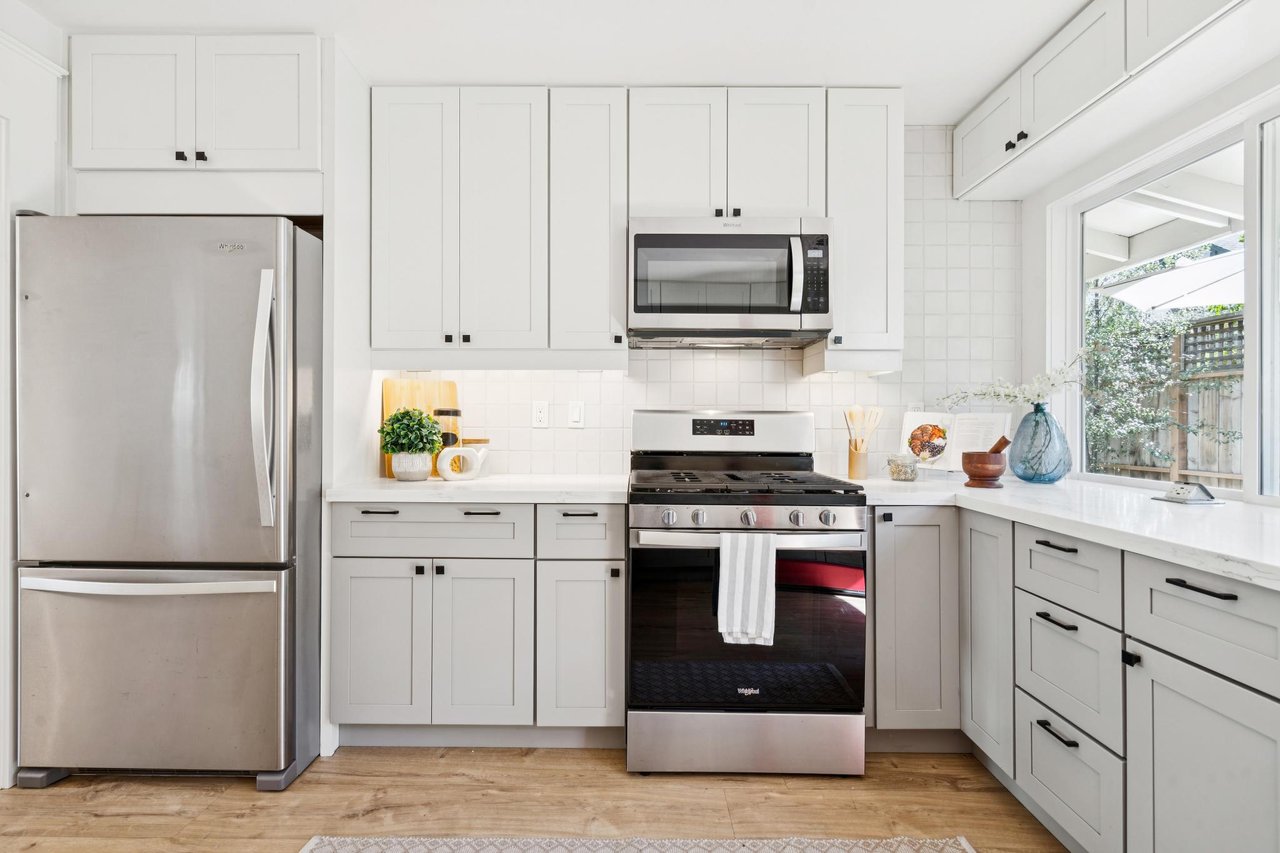 Bright white kitchen with stainless appliances and a large window overlooking a garden.