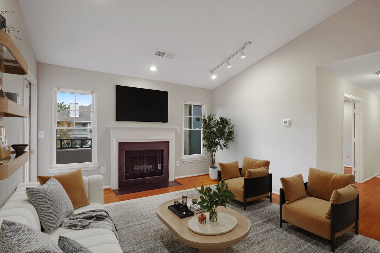 Staged living room with a fireplace, wall-mounted television, and tan-and-white seating.