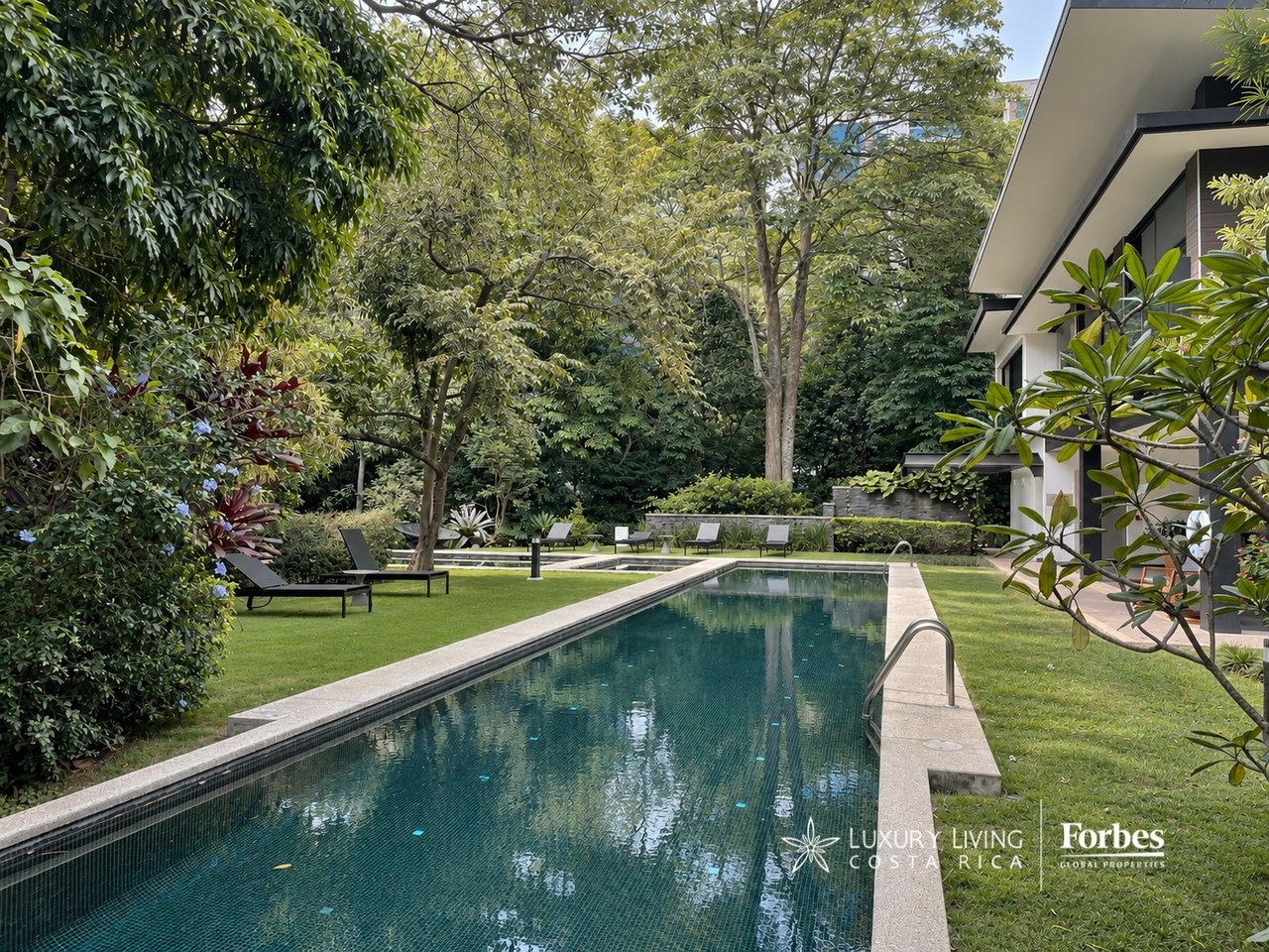 Apartment courtyard pool bordered by tropical landscaping, lawn, and lounge chairs.