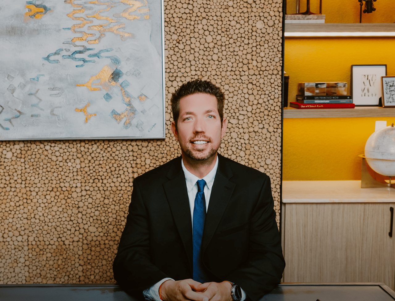 Chris Hitchcock seated in a black suit and blue tie against a wood-slice wall.