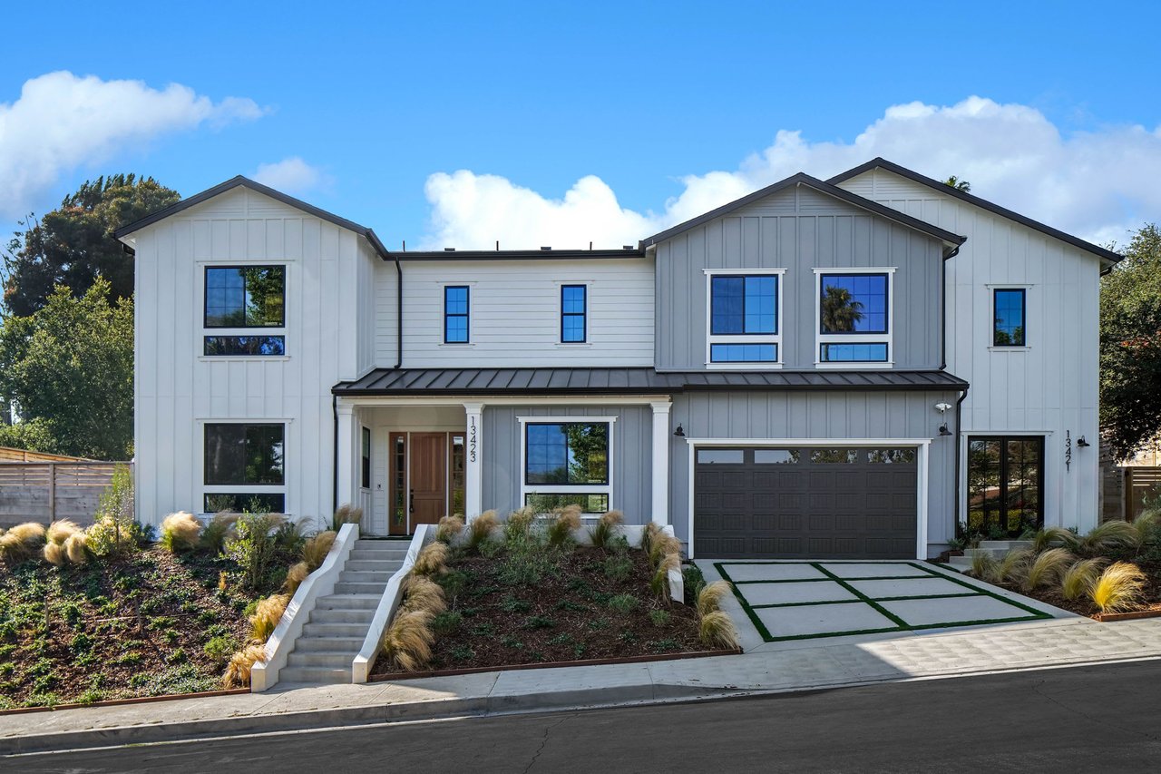  A grand two-story modern farmhouse-style house with a mix of light gray and white siding stands on a gentle slope 