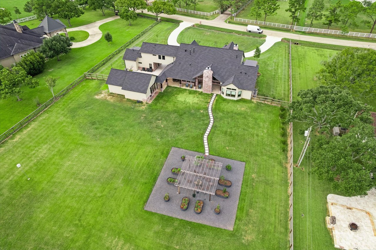 Aerial view of a large home and expansive fenced lawn, with a pergola patio and curved driveway.