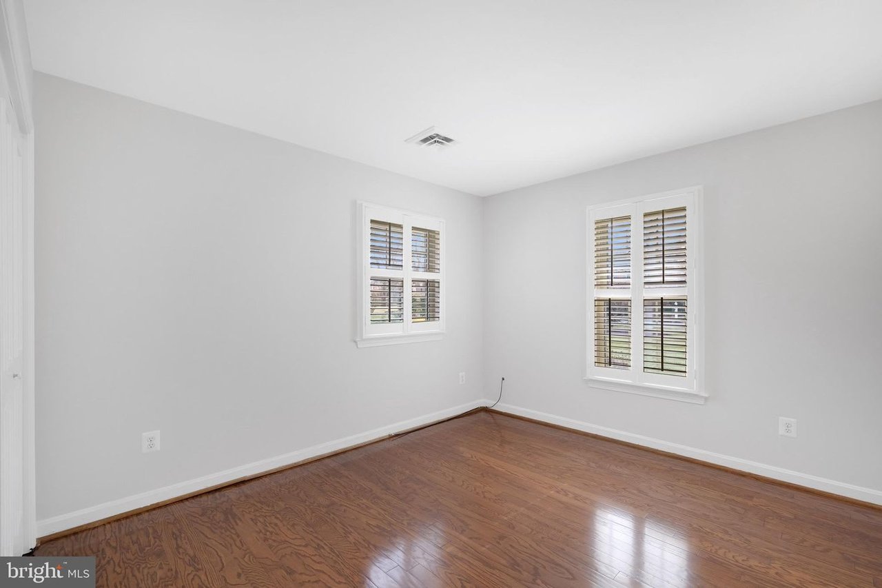 Vacant room with polished hardwood floors and two windows with plantation shutters.