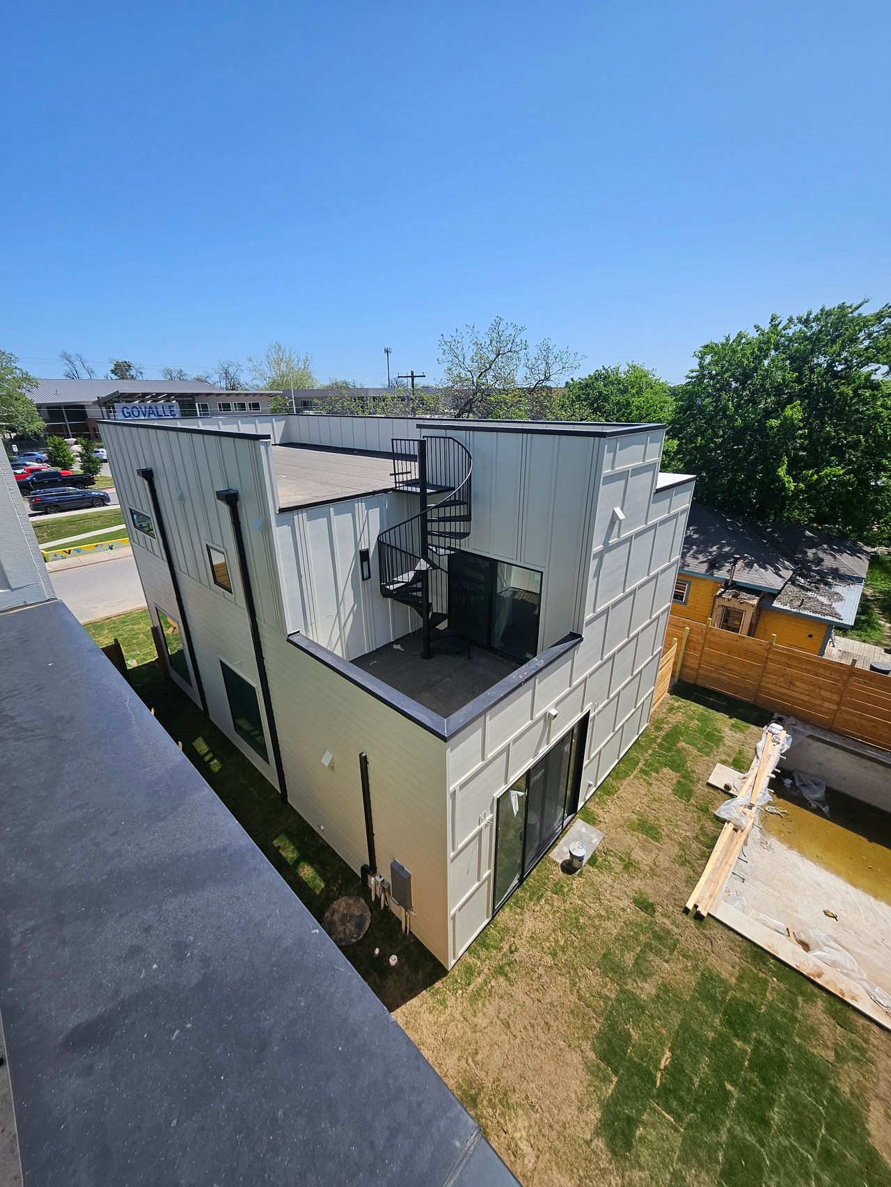 Modern multi-story building under construction with a rooftop terrace and black spiral staircase.