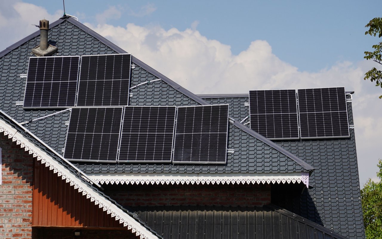 House with multiple solar panels across its dark tiled roof and brick exterior.