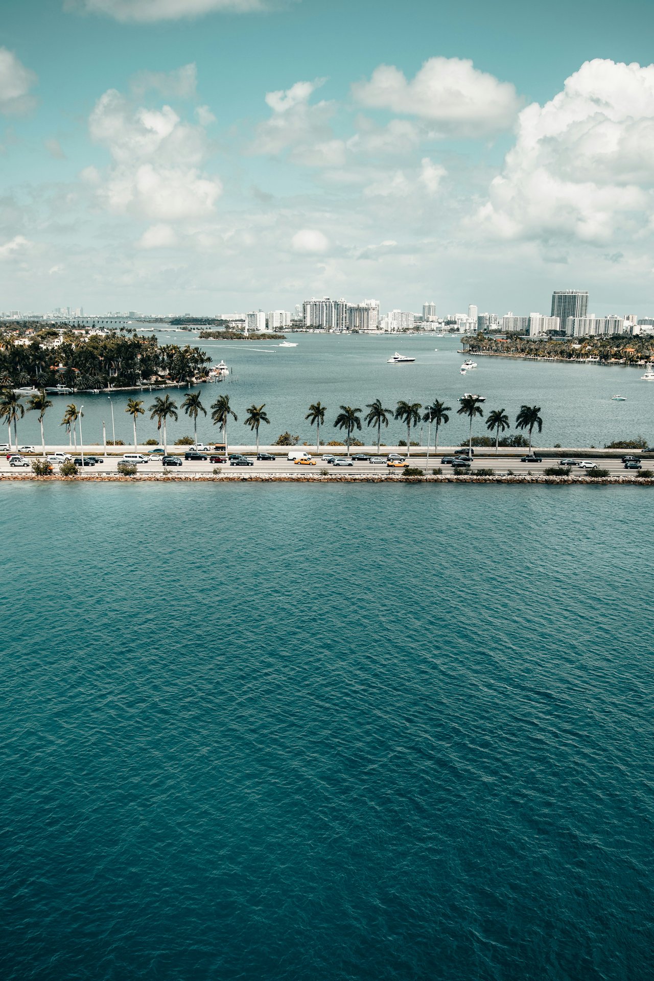 Miami skyline across Biscayne Bay, with yachts and a palm-lined causeway.
