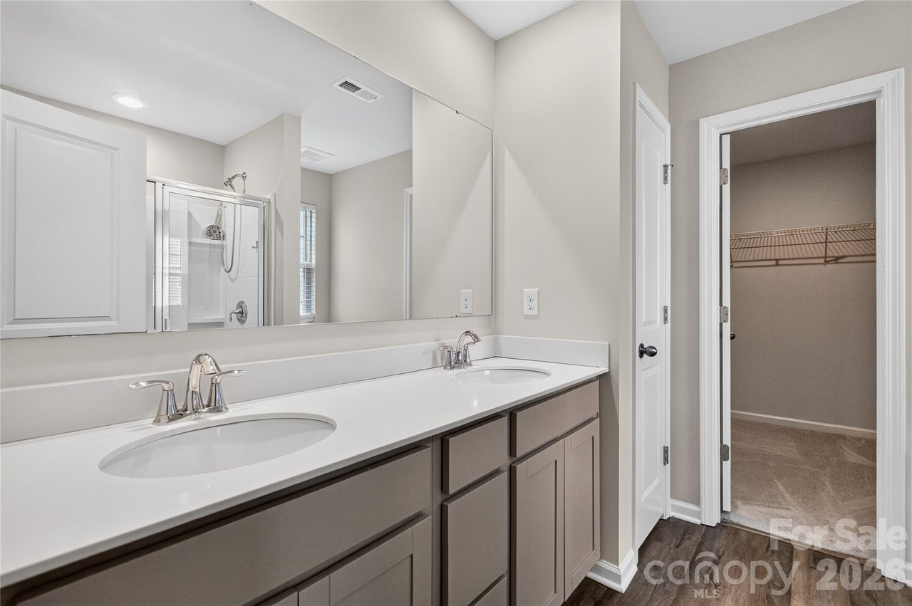 Bathroom with a double-sink vanity and mirror reflecting a glass shower; open doorway leads to a walk-in closet.
