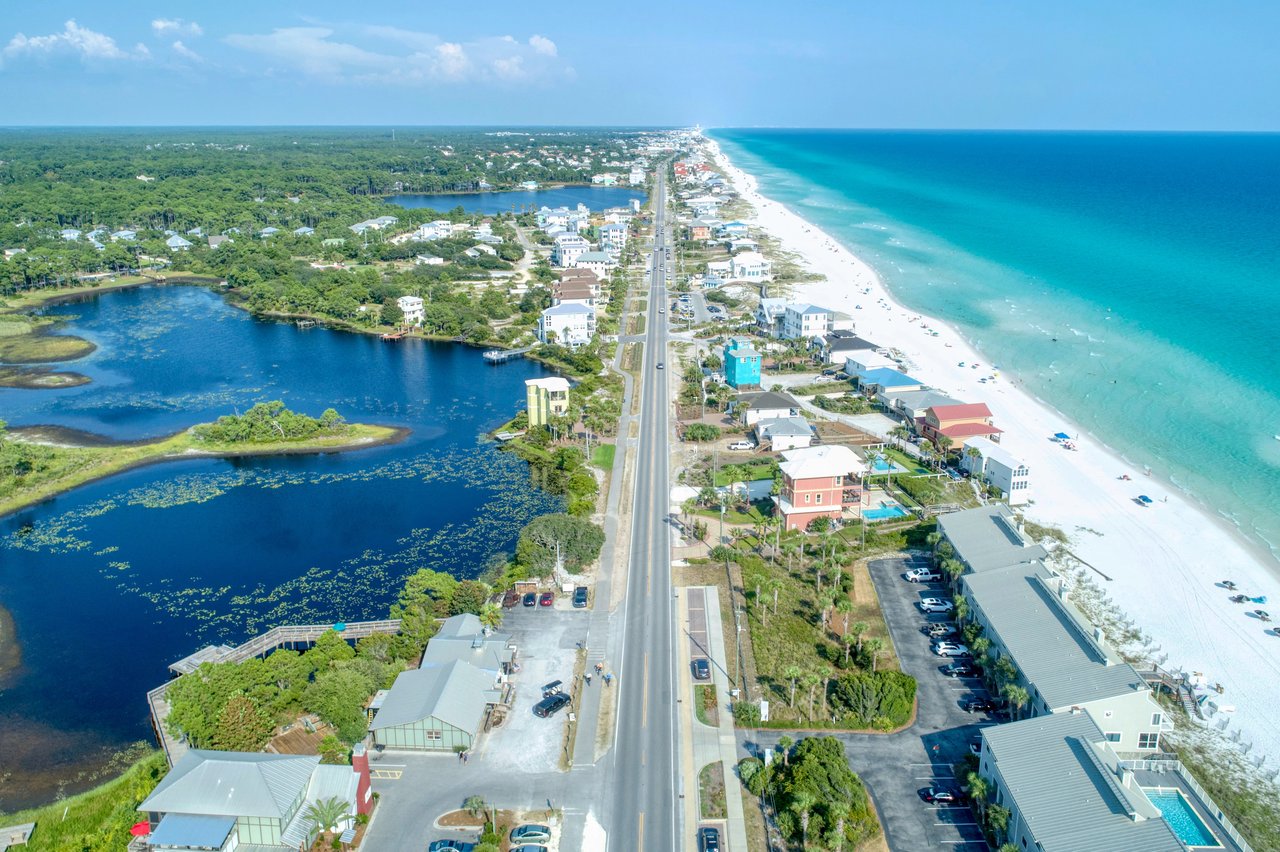 Aerial coastal community with a beachfront road, turquoise water, and inland lakes.