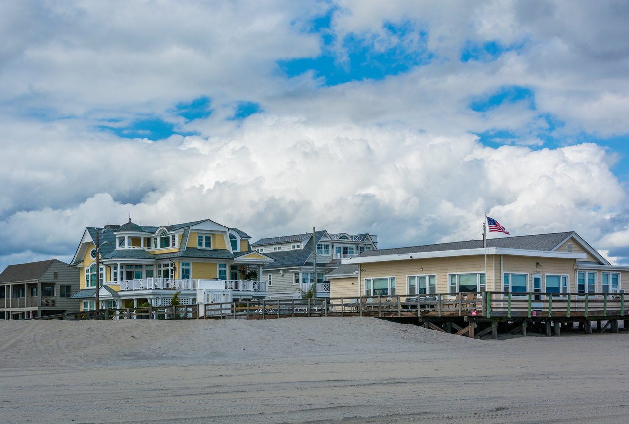 Coastal homes along a sandy beach, with a yellow house and raised boardwalk.