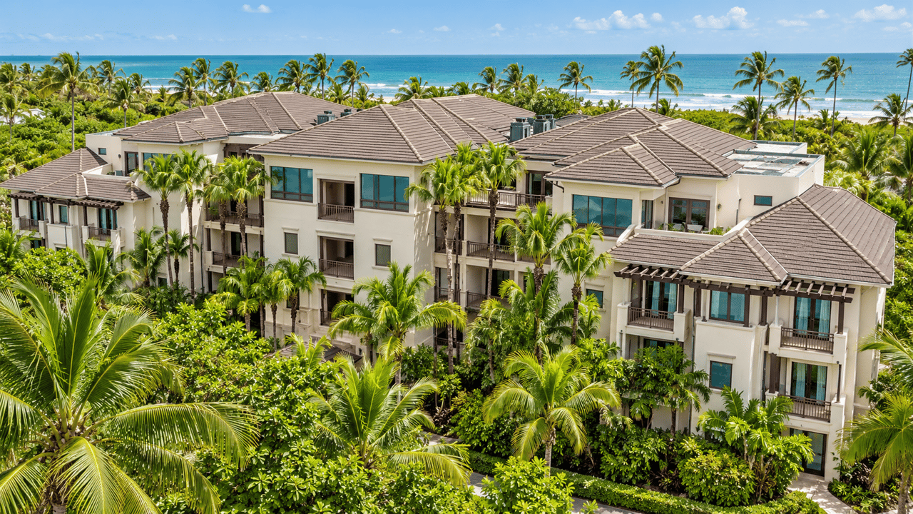 Aerial view of Las Ventanas condos amid palm trees, with the ocean and shoreline behind them.