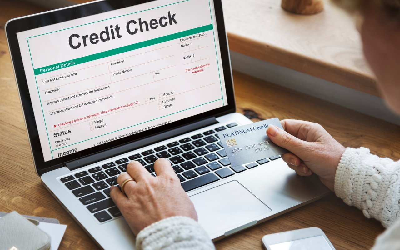 A person holds a credit card while completing a credit check form on a laptop.