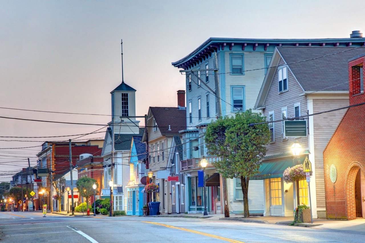 Small-town street at dusk with colorful storefronts and a church steeple.