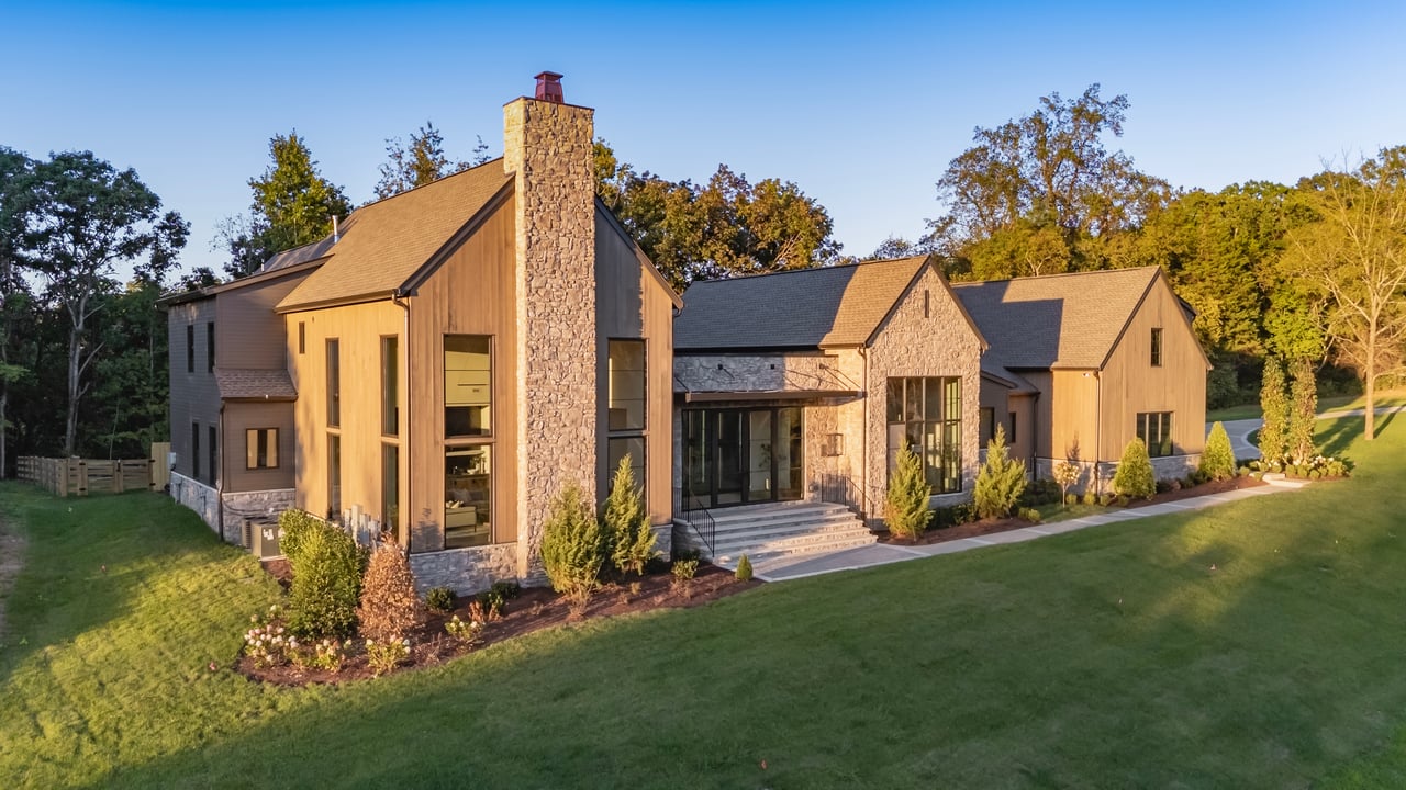 Modern timber-and-stone home with a tall stone chimney, landscaped grounds, and a broad lawn.