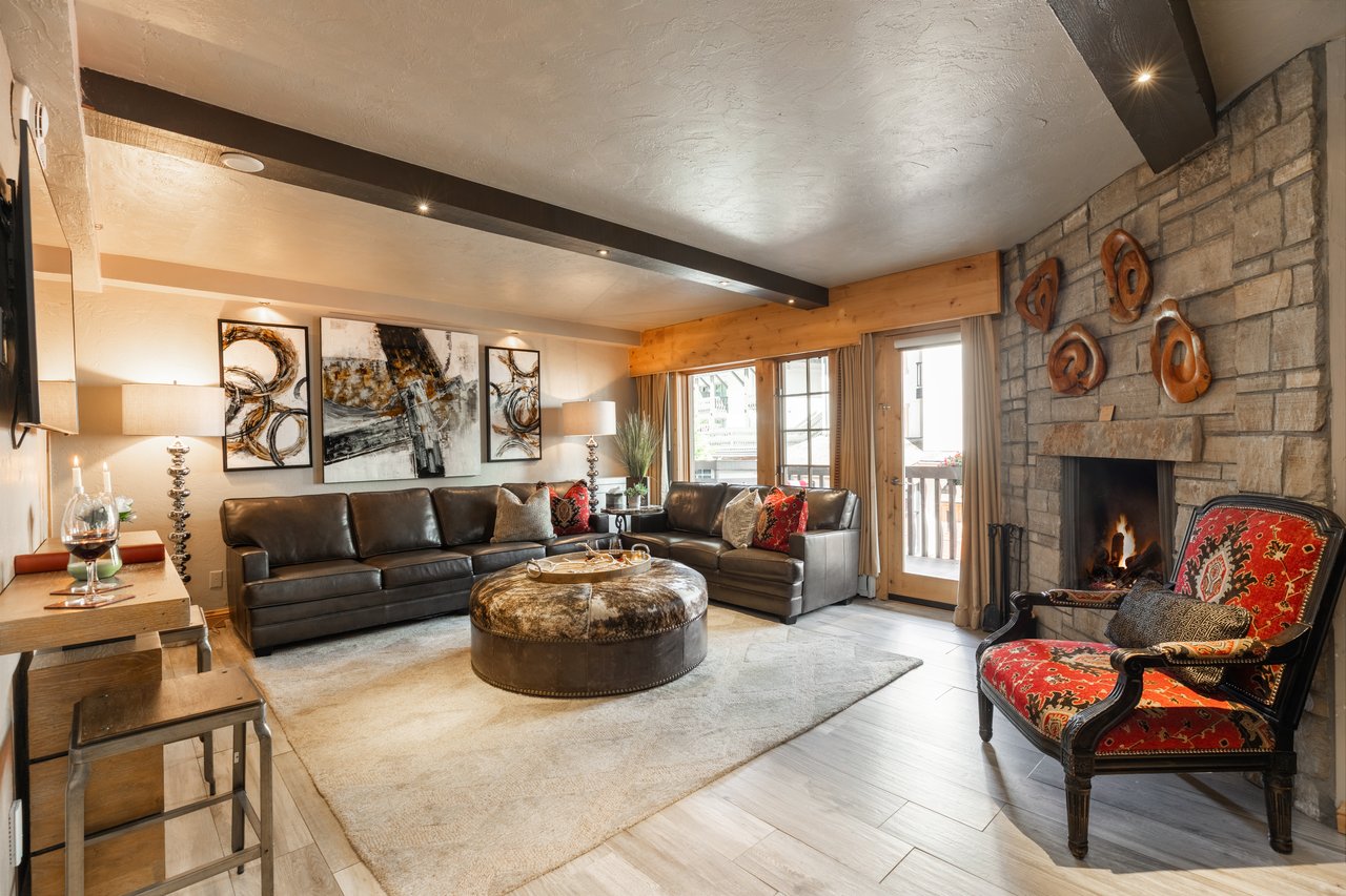 Living room with a leather sectional, stone fireplace, and red patterned accent chair.
