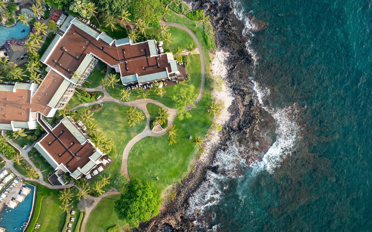 Aerial view of beachfront residences at Niu Beach, with palm-lined lawns and a rocky shoreline.