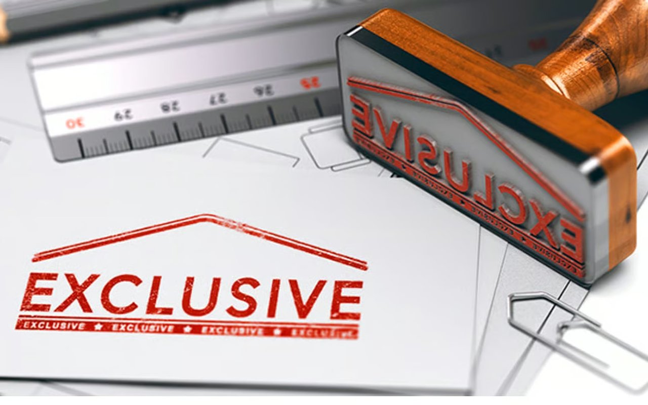 A wooden-handled stamp and ruler beside an “EXCLUSIVE” imprint on real estate paperwork.