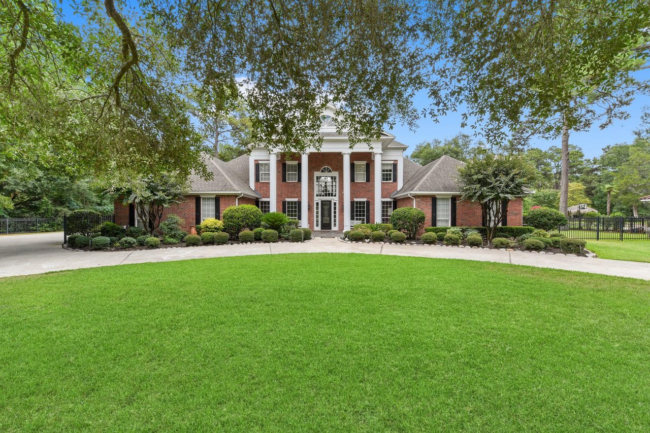 Two-story brick home with white columns, landscaped shrubs, and a broad green lawn.