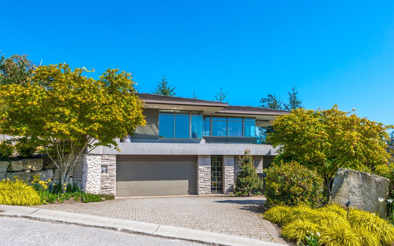 A modern house with a large driveway, garage door, and trees in front of it.