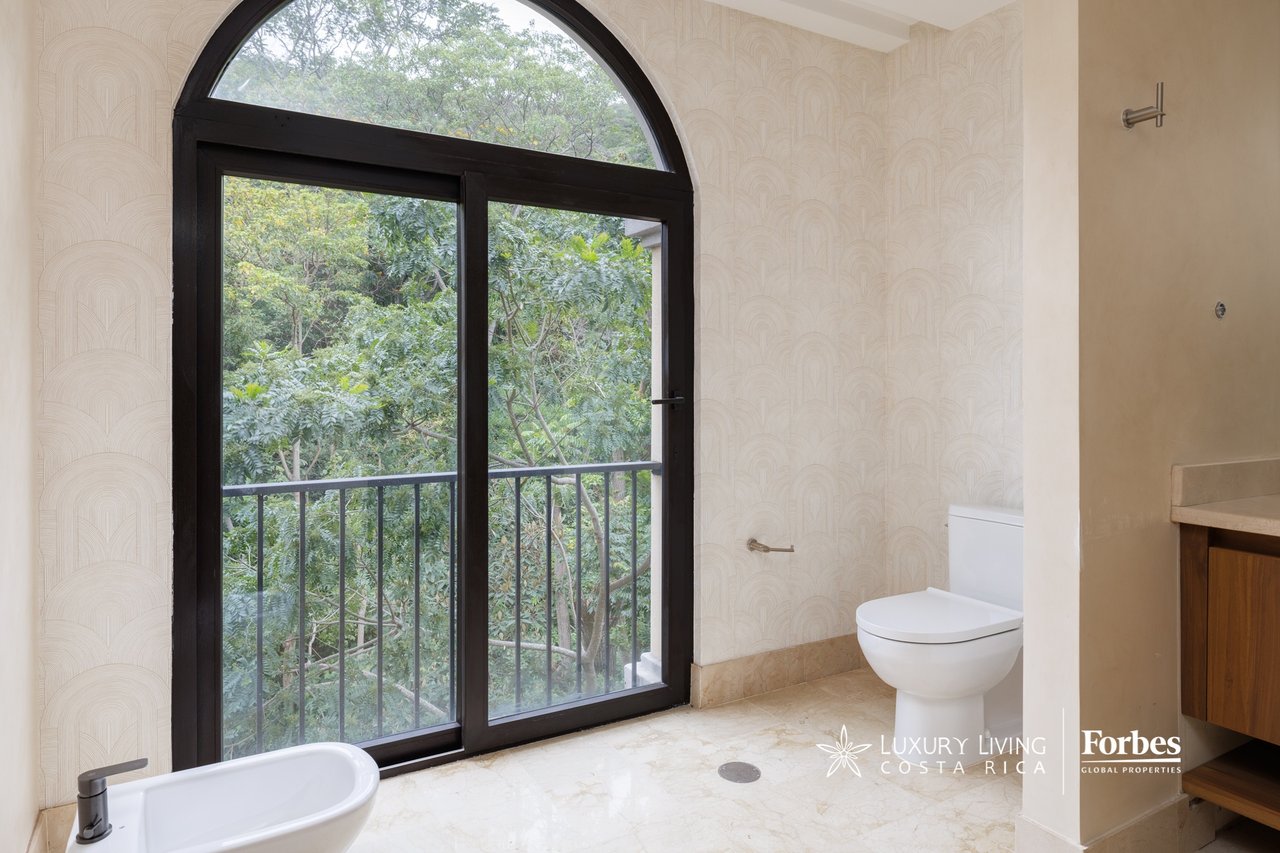 Bathroom with arched glass doors opening to a tree-lined balcony and a partially visible bathtub.