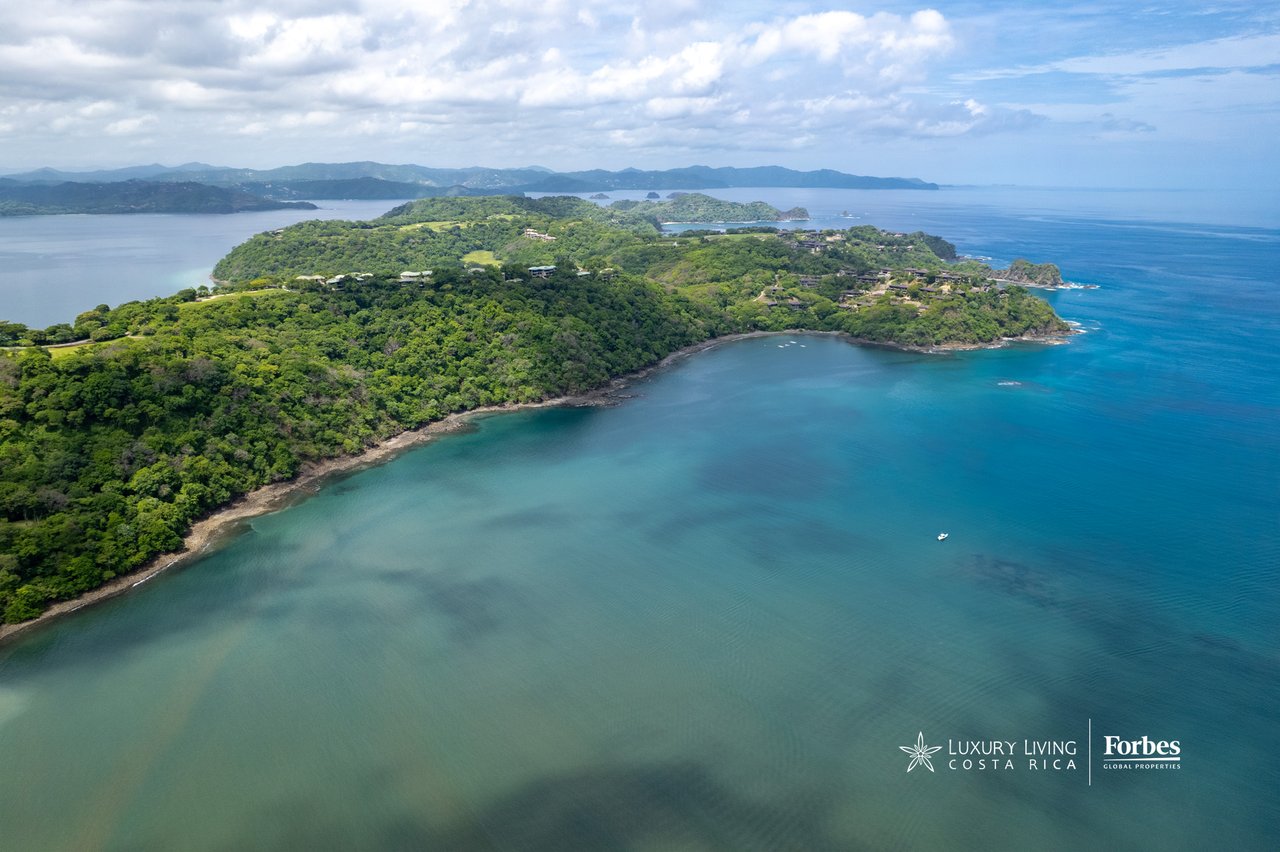 Aerial view of a forested peninsula surrounded by turquoise bays and ocean.
