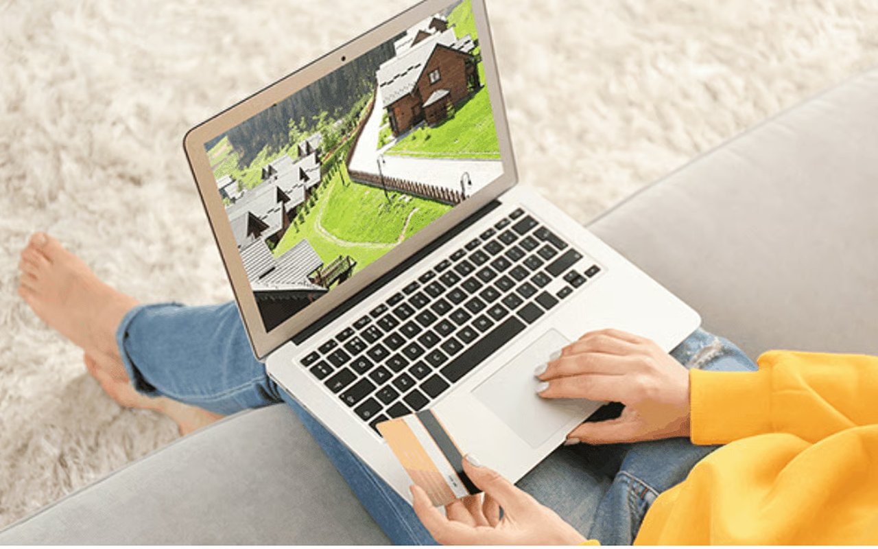Person views houses on a laptop while holding a payment card.
