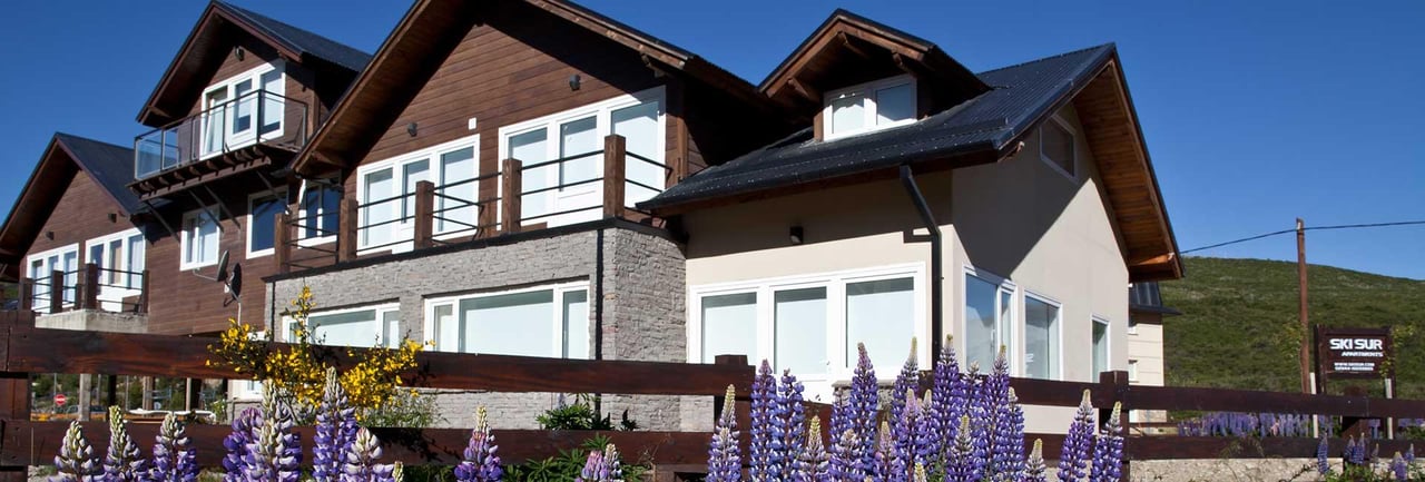 Ski Sur chalet with wood-and-stone facade, balconies, and purple flowers along the front fence.