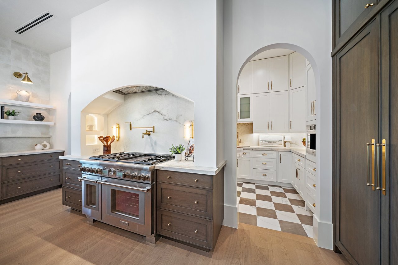 Luxury kitchen with a stainless gas range, arched marble backsplash, and checkerboard-floor butler’s pantry.
