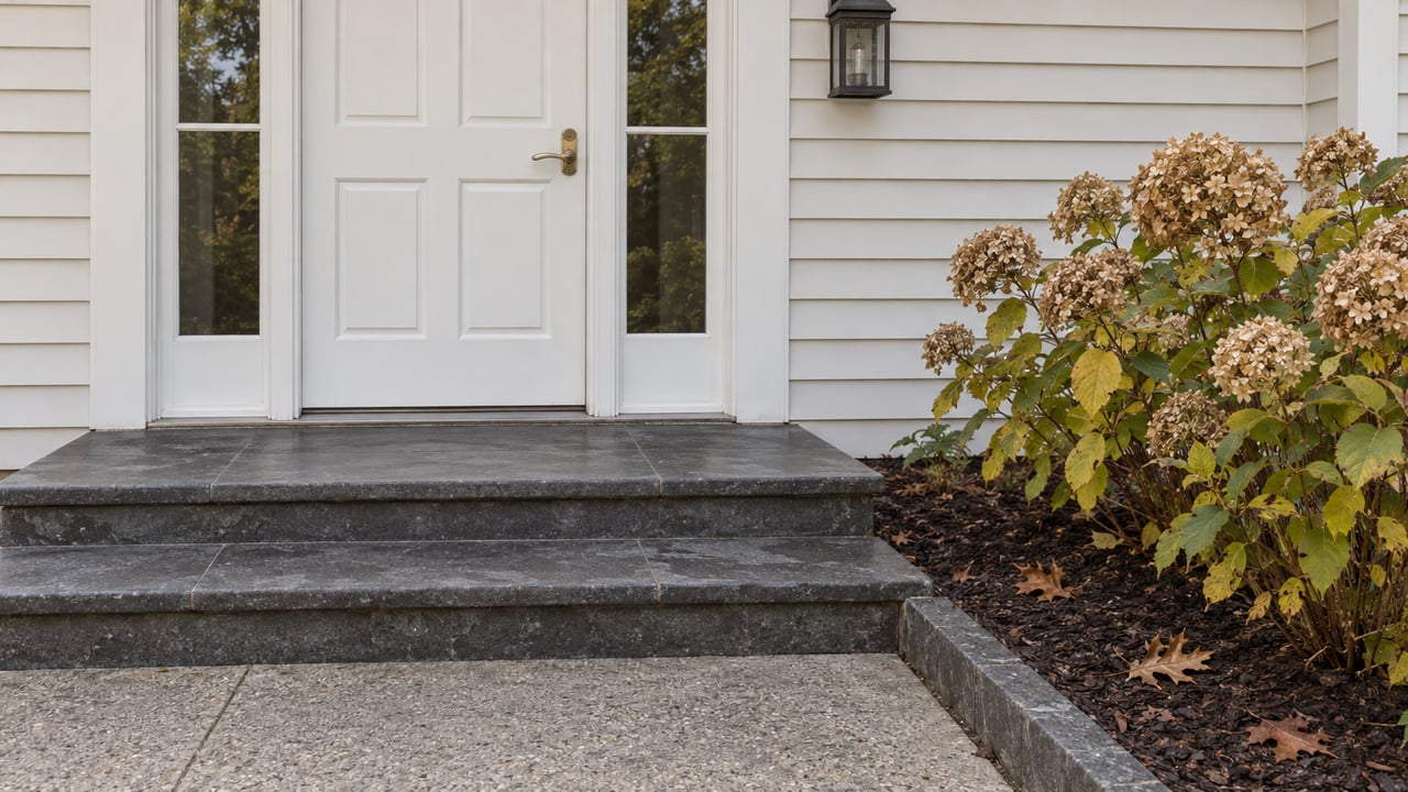 White paneled entrance with paired sidelights, charcoal stone steps and a hydrangea with tan autumn flower heads.